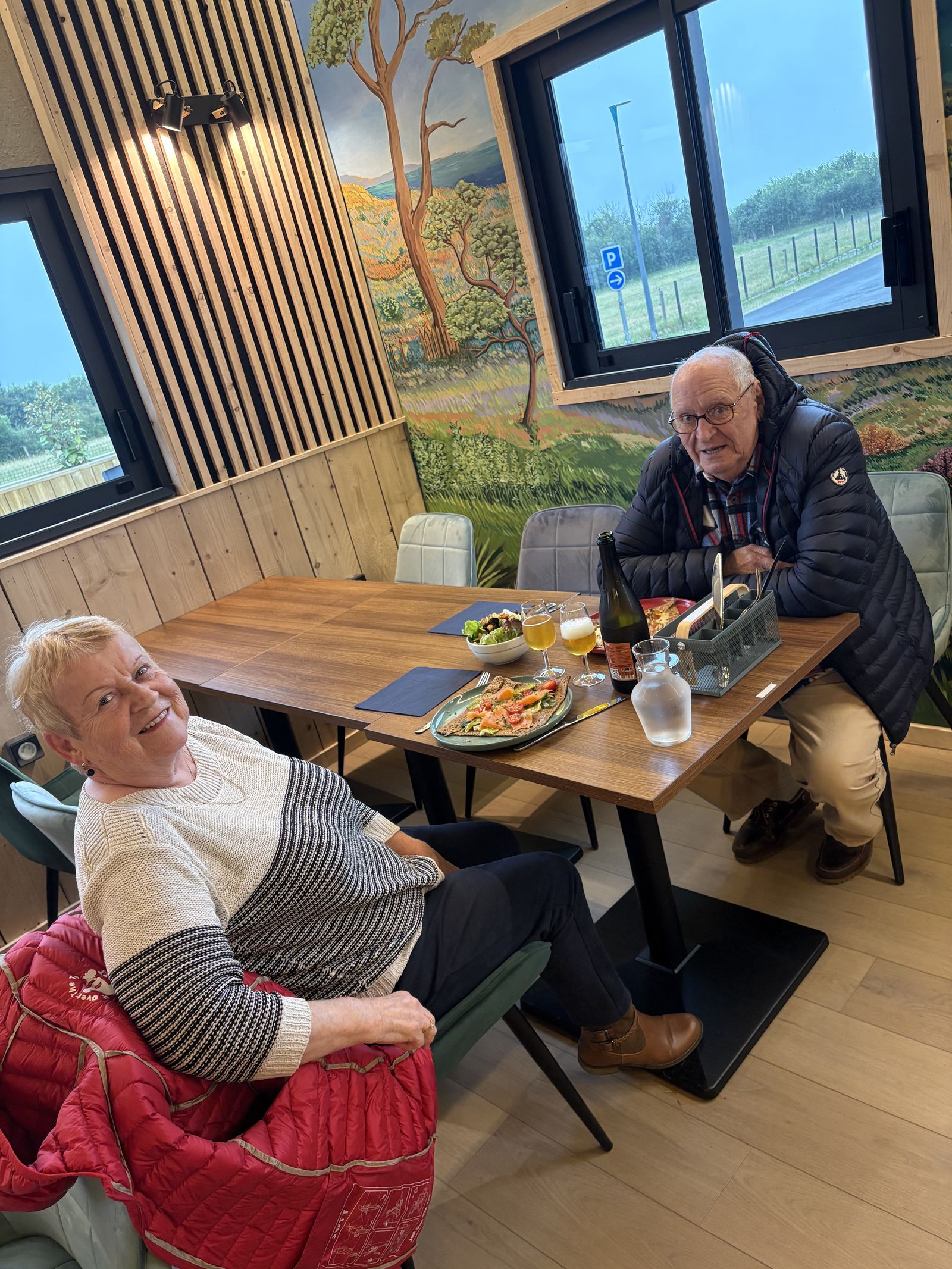 Two smiling guests at their table in the dining room, in front of the dune mural.