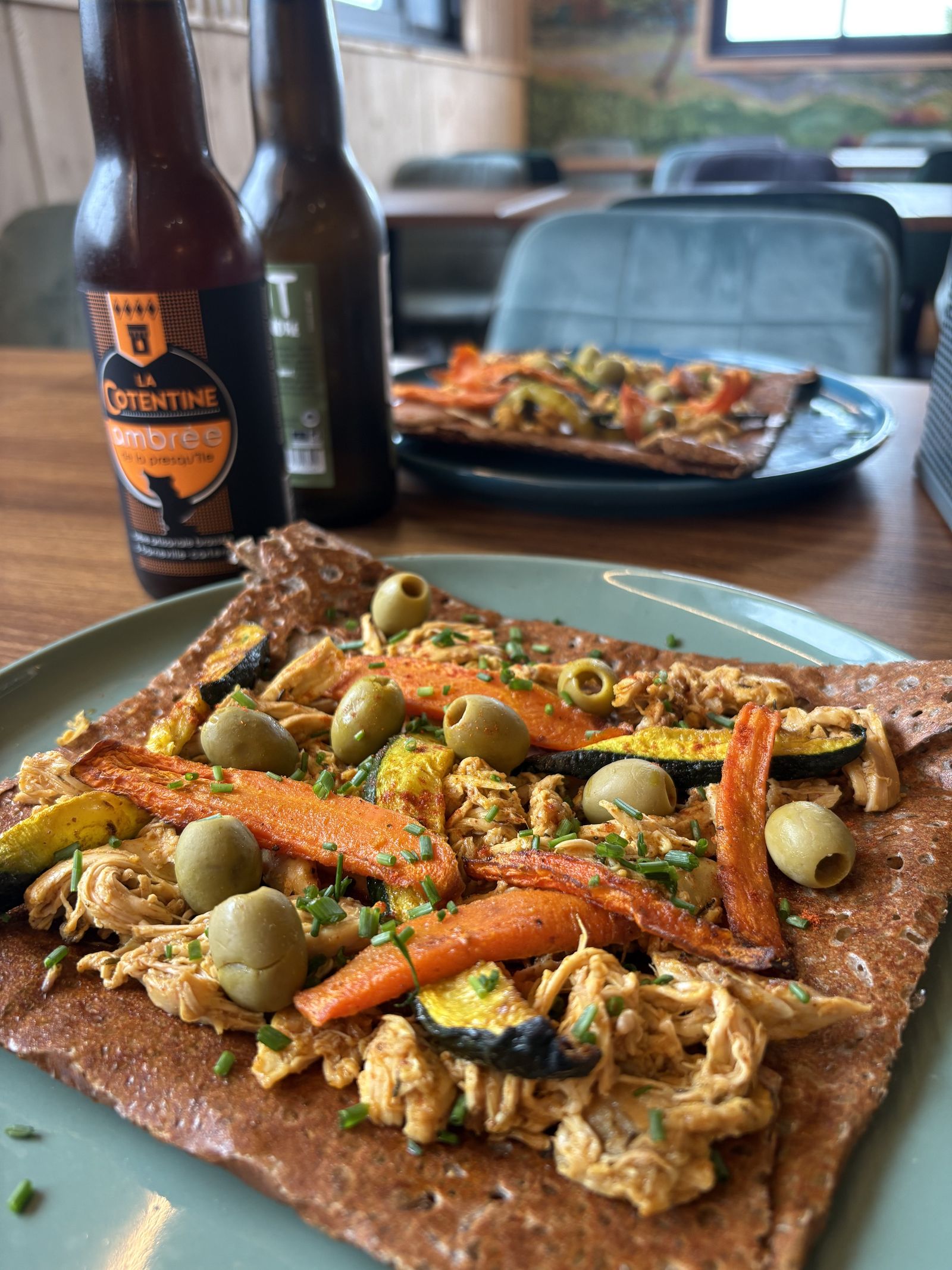Close-up of a buckwheat galette topped with roasted vegetables, olives and chicken.