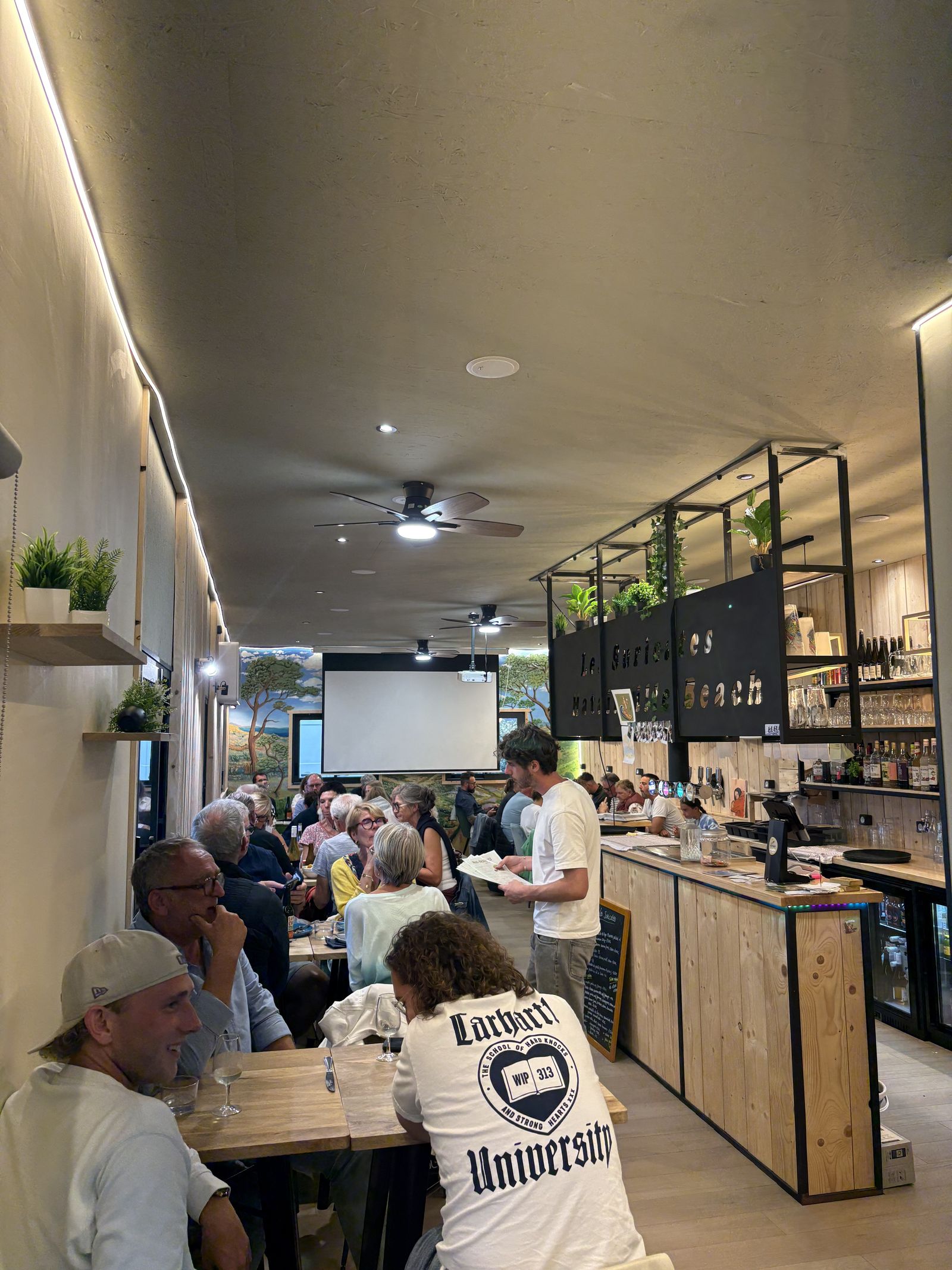 The busy dining room, the long wooden counter and guests at their tables.