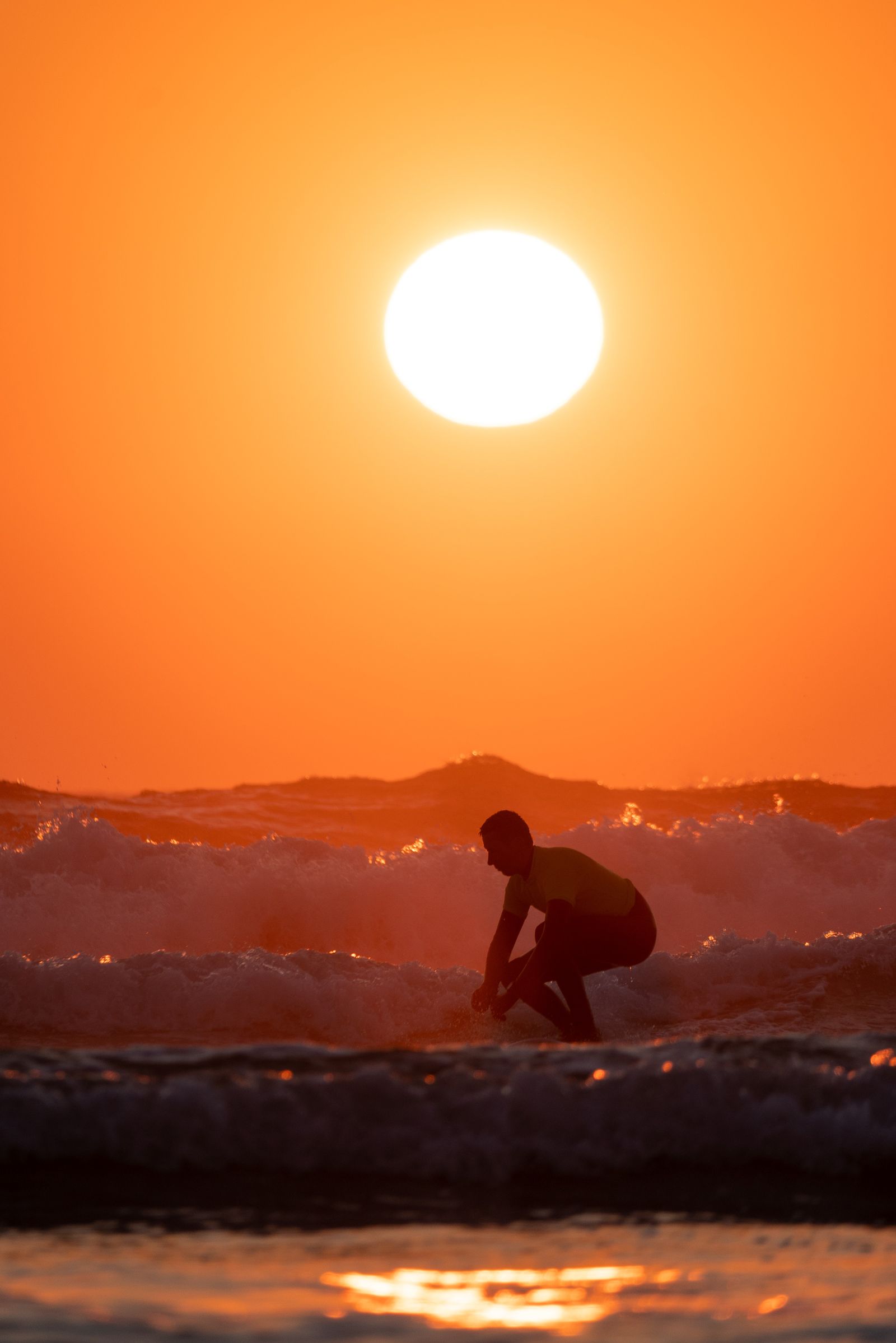 A surfer silhouetted in the waves at sunset, on Hatainville beach.