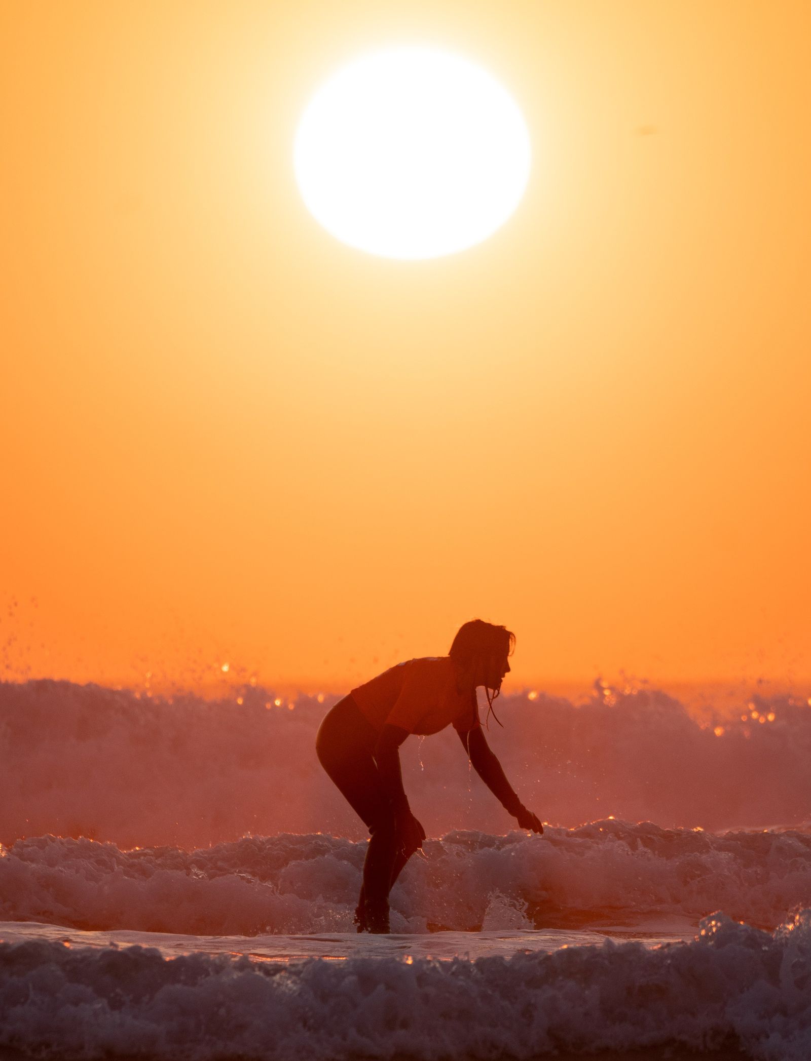 A surfer silhouetted in the waves at sunset.