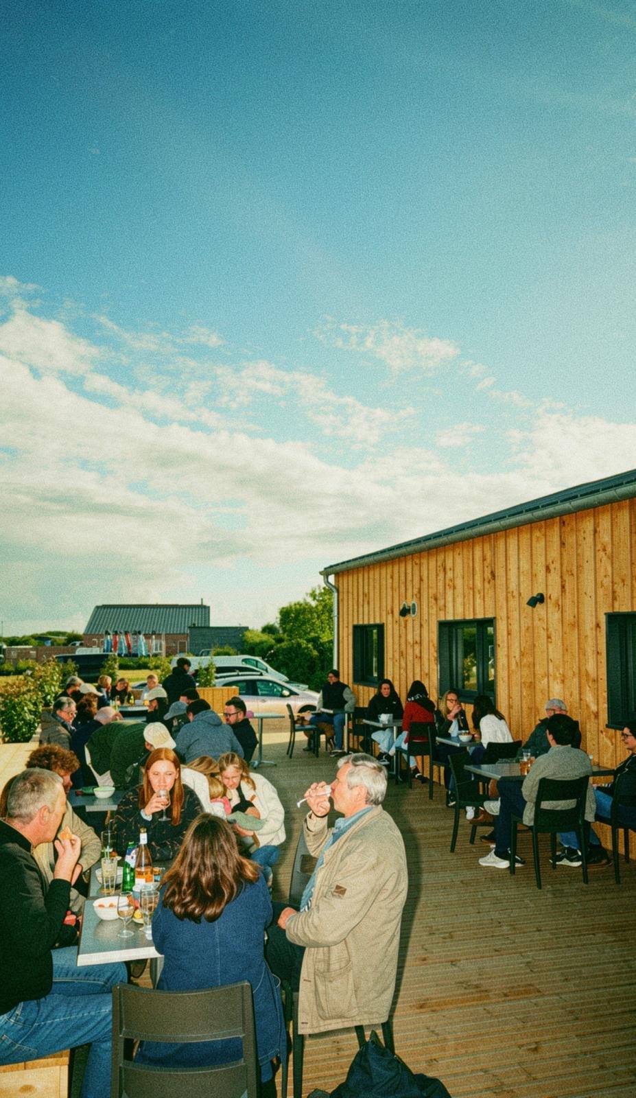 The Les Suricates terrace on a fine evening: guests at their tables on the wooden deck, in front of the timber-clad building.